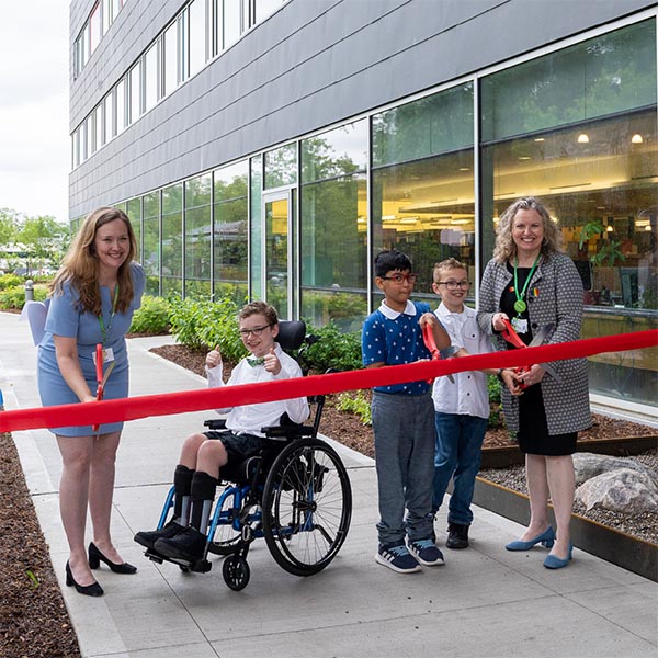 Two adults and three children (one child on wheelchair) in a ribbon cutting ceremony